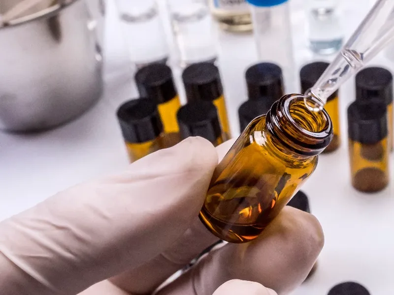 Gloved hand filling an amber fragrance vial with a pipette